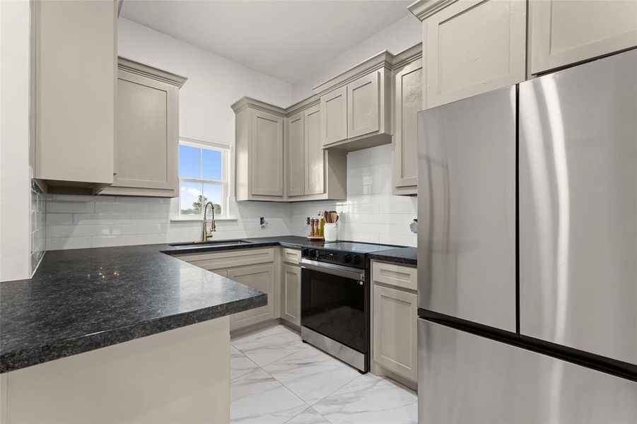 Kitchen with freestanding refrigerator, electric range, light marble finish floors, dark countertops, and backsplash