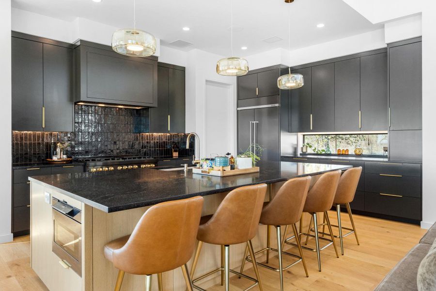 Gourmet kitchen featuring dark cabinetry, a large kitchen island with integrated microwave, black tile backsplash, and light wood-finish flooring