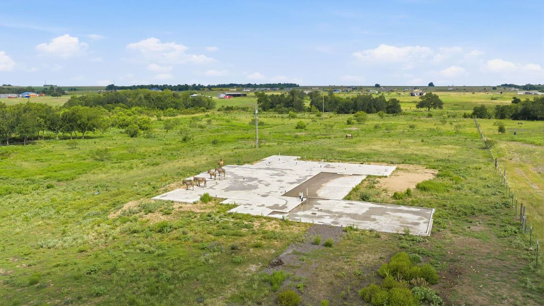 A rural setting with verdant fields surrounds a newly poured concrete foundation, awaiting a dream home.