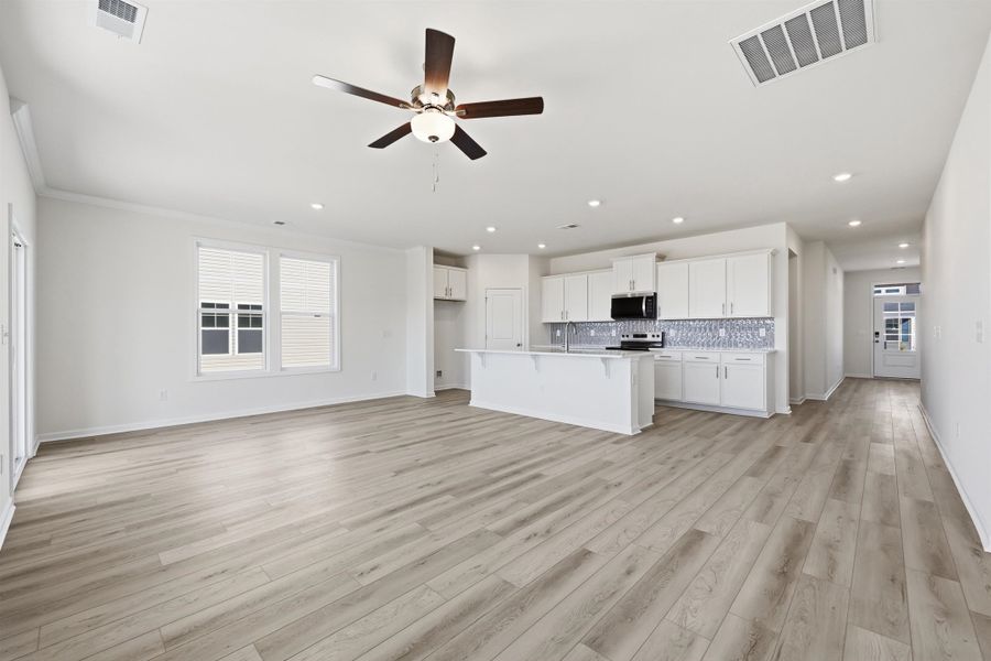 Kitchen with open floor plan, a kitchen breakfast bar, white cabinets, a kitchen island with sink, and a ceiling fan
