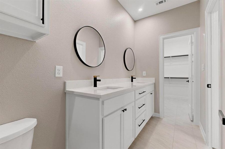 Bathroom featuring double vanity, a spacious closet, light tile patterned floors, and a textured wall Bathroom featuring double vanity, a spacious closet, light tile patterned floors, and a textured wall