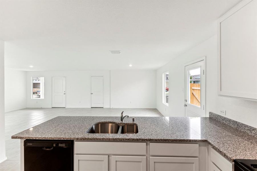 Kitchen with light tile patterned flooring, kitchen peninsula, dishwasher, stone counters, and sink