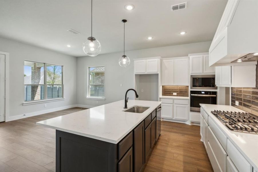 Kitchen with a kitchen island with sink, stainless steel appliances, light hardwood / wood-style floors, and tasteful backsplash