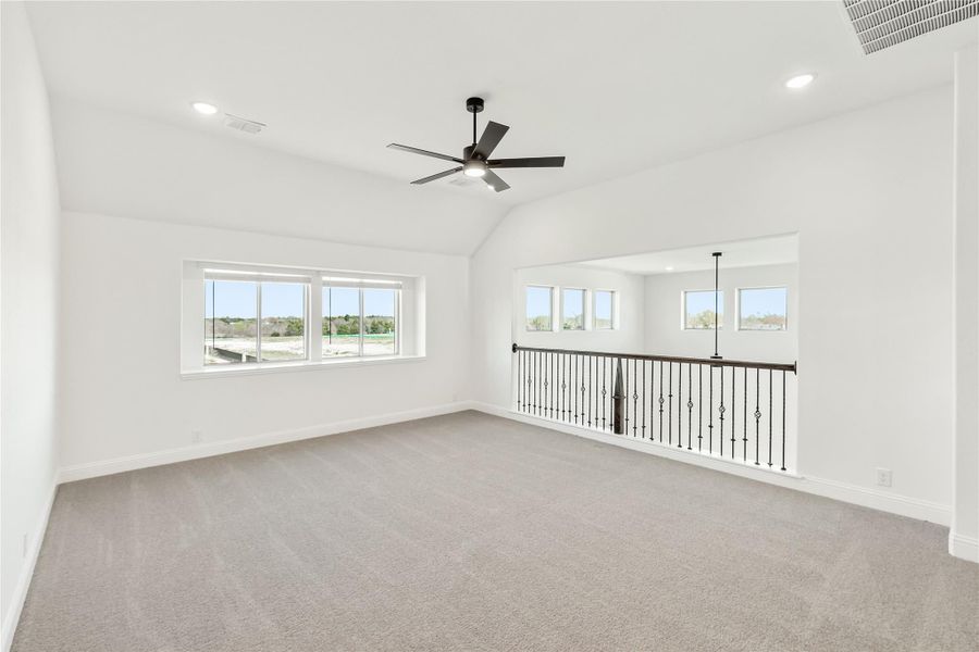 Open upstairs bonus room with vaulted ceiling, ceiling fan, carpet, and iron stair railing overlooking lower level Open upstairs bonus room with vaulted ceiling, ceiling fan, carpet, and iron stair railing overlooking lower level