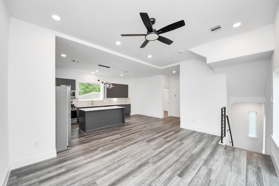This modern open-concept living space features sleek wood flooring, a stylish ceiling fan, and recessed lighting. The kitchen boasts dark cabinets, stainless steel appliances, and a large central island, providing a contemporary and functional design. This modern open-concept living space features sleek wood flooring, a stylish ceiling fan, and recessed lighting. The kitchen boasts dark cabinets, stainless steel appliances, and a large central island, providing a contemporary and functional design.