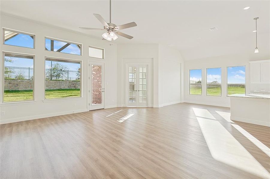 Unfurnished living room featuring french doors, a glass covered fireplace, light wood finished floors, ceiling fan, and a high ceiling Unfurnished living room featuring french doors, a glass covered fireplace, light wood finished floors, ceiling fan, and a high ceiling