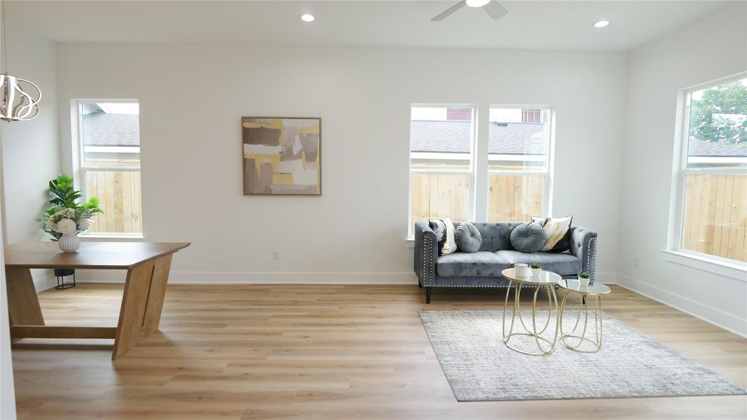 Bright and airy living space with large windows, light wood flooring, and recessed lighting. Features a cozy gray sofa, modern artwork, and a stylish wood dining table, creating a welcoming atmosphere. Bright and airy living space with large windows, light wood flooring, and recessed lighting. Features a cozy gray sofa, modern artwork, and a stylish wood dining table, creating a welcoming atmosphere.