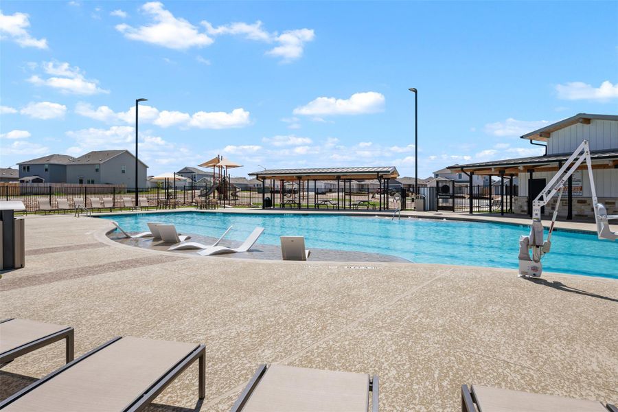 An expansive community swimming pool is surrounded by spacious concrete decking under clear blue skies. An expansive community swimming pool is surrounded by spacious concrete decking under clear blue skies.