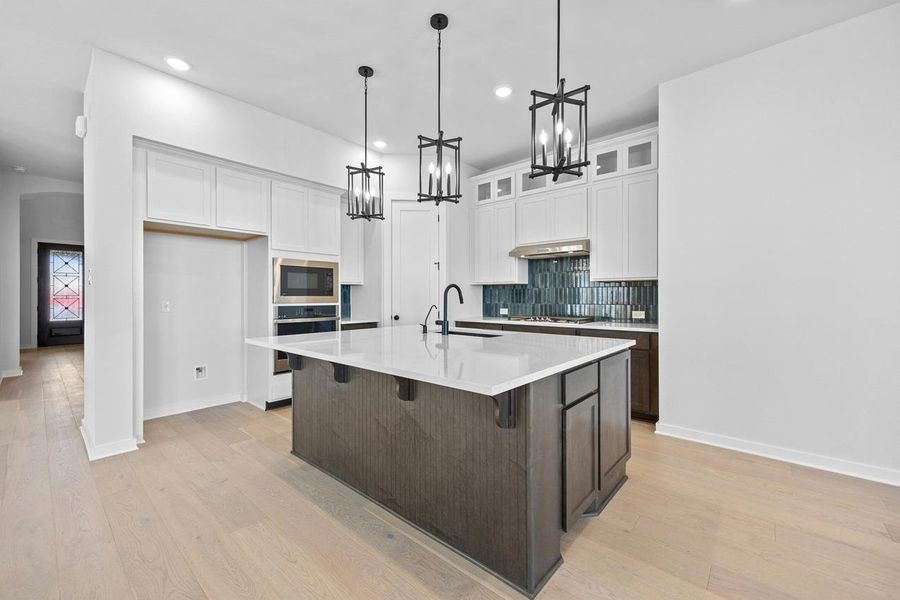 Kitchen with stainless steel oven, a chandelier, black microwave, tasteful backsplash, and white cabinets Kitchen with stainless steel oven, a chandelier, black microwave, tasteful backsplash, and white cabinets