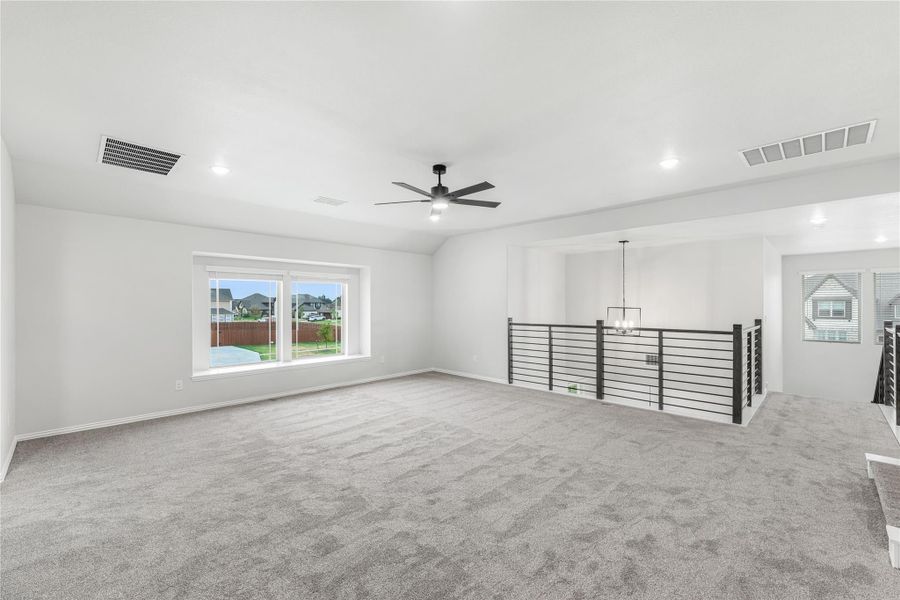 Spacious upstairs bonus room with gray carpet, ceiling fan, and open metal railing overlooking staircase