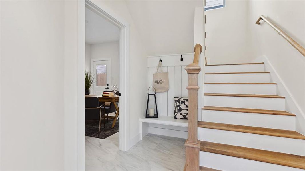 As you step into your bright, modern entryway with a staircase, you are greeted with stone tiled flooring, wooden custom handrails with white risers, leading to the upper second level. There's a glimpse into your well-lit secondary room with private en-suite bathroom.