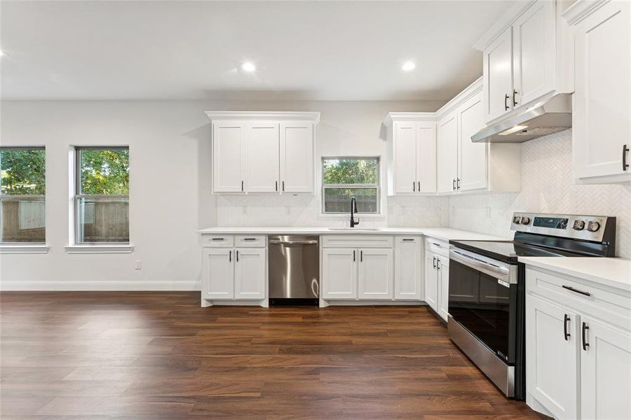 Kitchen featuring appliances with stainless steel finishes, tasteful backsplash, white cabinets, under cabinet range hood, and recessed lighting