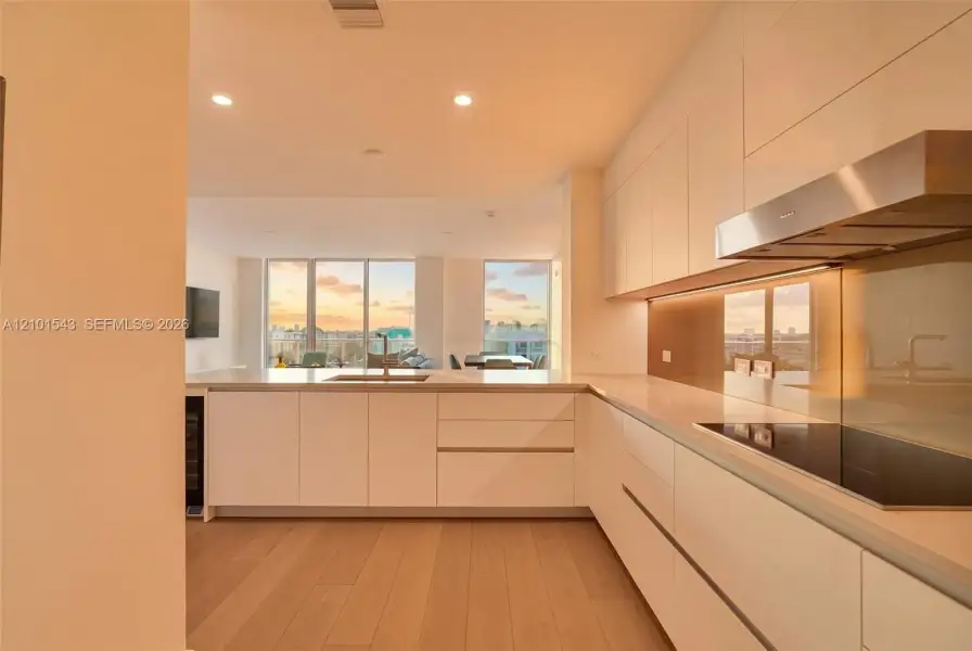 Contemporary kitchen featuring flat-panel cabinetry, light-toned wood-finish flooring, a stainless steel range hood, an integrated cooktop, and floor-to-ceiling windows