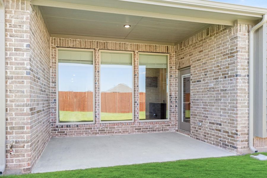 Covered back patio with concrete floor, brick exterior walls, and large windows overlooking a fenced backyard. Covered back patio with concrete floor, brick exterior walls, and large windows overlooking a fenced backyard.