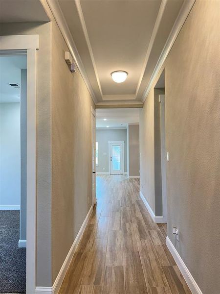 Hallway featuring wood-finish flooring, tray ceiling with recessed lighting, and crisp white baseboards