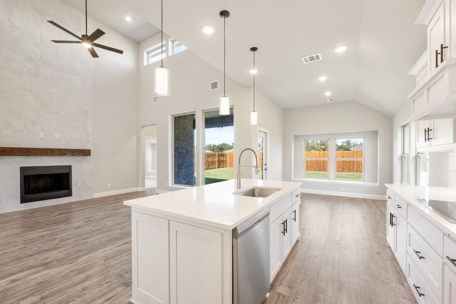 Open kitchen with white cabinets, center island, and vaulted ceiling open to living room with fireplace Open kitchen with white cabinets, center island, and vaulted ceiling open to living room with fireplace