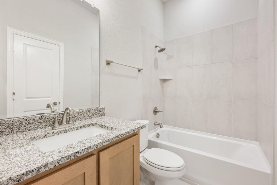 Bathroom with granite countertop vanity, toilet, and tiled shower-tub combo with brushed nickel fixtures