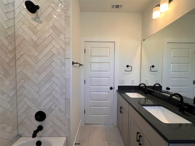 Full bath with double vanity, bathtub / shower combination, and light tile patterned flooring