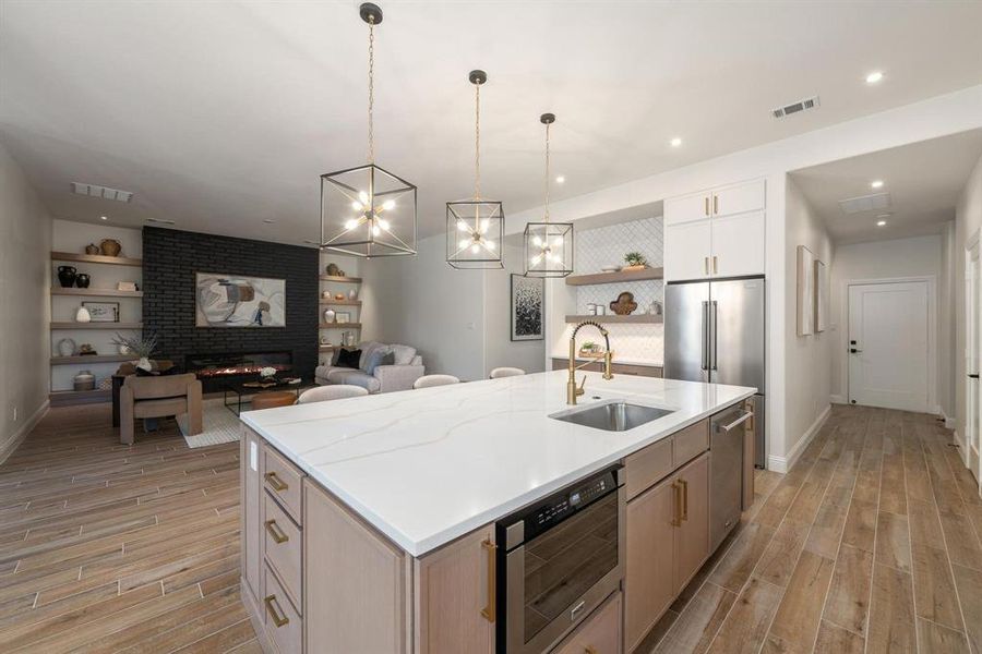 Kitchen with wood tiled floors, hanging light fixtures, open floor plan, a kitchen island with sink, and a brick fireplace Kitchen with wood tiled floors, hanging light fixtures, open floor plan, a kitchen island with sink, and a brick fireplace