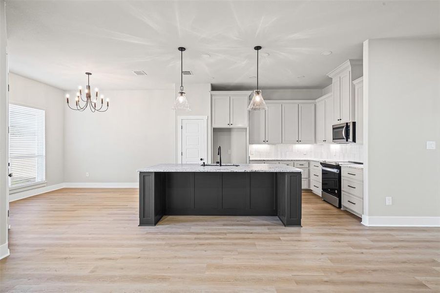 Kitchen featuring white cabinets, appliances with stainless steel finishes, a kitchen island with sink, pendant lighting, and light wood-style floors Kitchen featuring white cabinets, appliances with stainless steel finishes, a kitchen island with sink, pendant lighting, and light wood-style floors