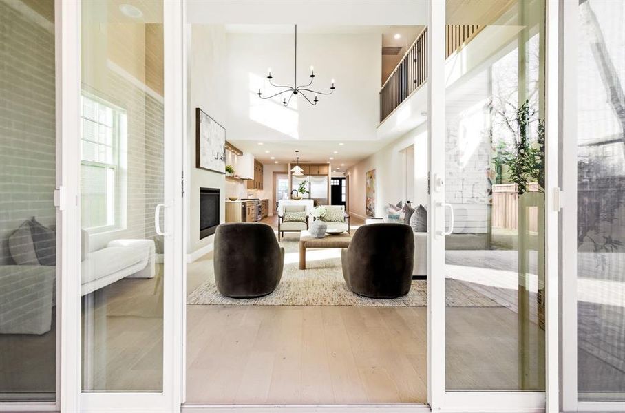 Living room featuring light wood-style floors, suspended lighting, a high ceiling, and a glass covered fireplace
