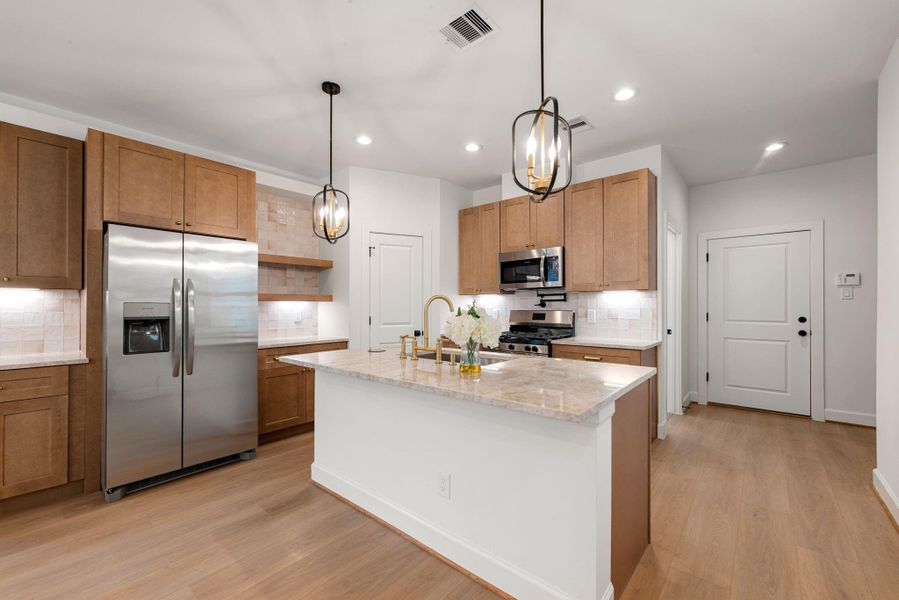 Stylish open kitchen featuring warm wood cabinetry, quartz countertops, and a large center island with seating. Stainless steel appliances, designer pendant lighting, and a sleek tile backsplash complete this bright and functional space, perfect for cooking and entertaining.