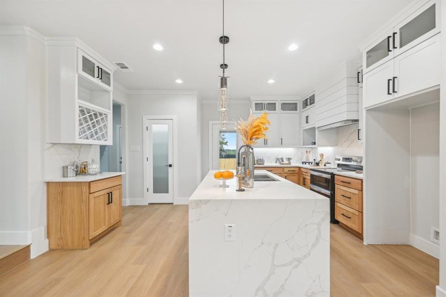 Kitchen with decorative light fixtures, light hardwood / wood-style floors, white cabinetry, a center island with sink, and stainless steel range with electric cooktop