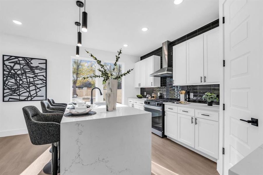 Kitchen with wall chimney exhaust hood, decorative light fixtures, light hardwood / wood-style flooring, stainless steel range with gas cooktop, and an island with sink