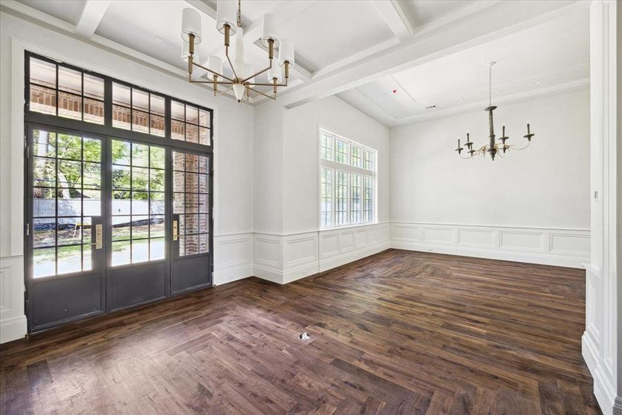 Behind the seating area is a spacious primary bedroom with beautiful floors, wood wall paneling, and an antique chandelier.