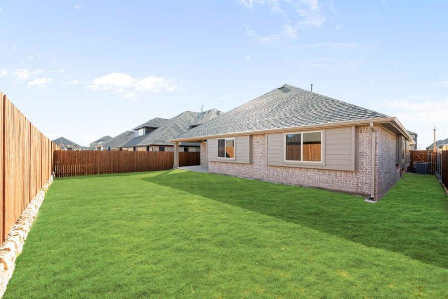 Backyard of single-story brick home with green lawn, wood privacy fence, and covered patio area. Backyard of single-story brick home with green lawn, wood privacy fence, and covered patio area.