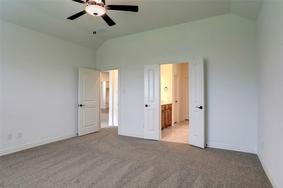 Unfurnished bedroom with high vaulted ceiling, ceiling fan, light carpet, and ensuite bathroom