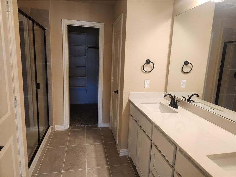 Bathroom featuring a shower with shower door, tile patterned flooring, and double sink vanity