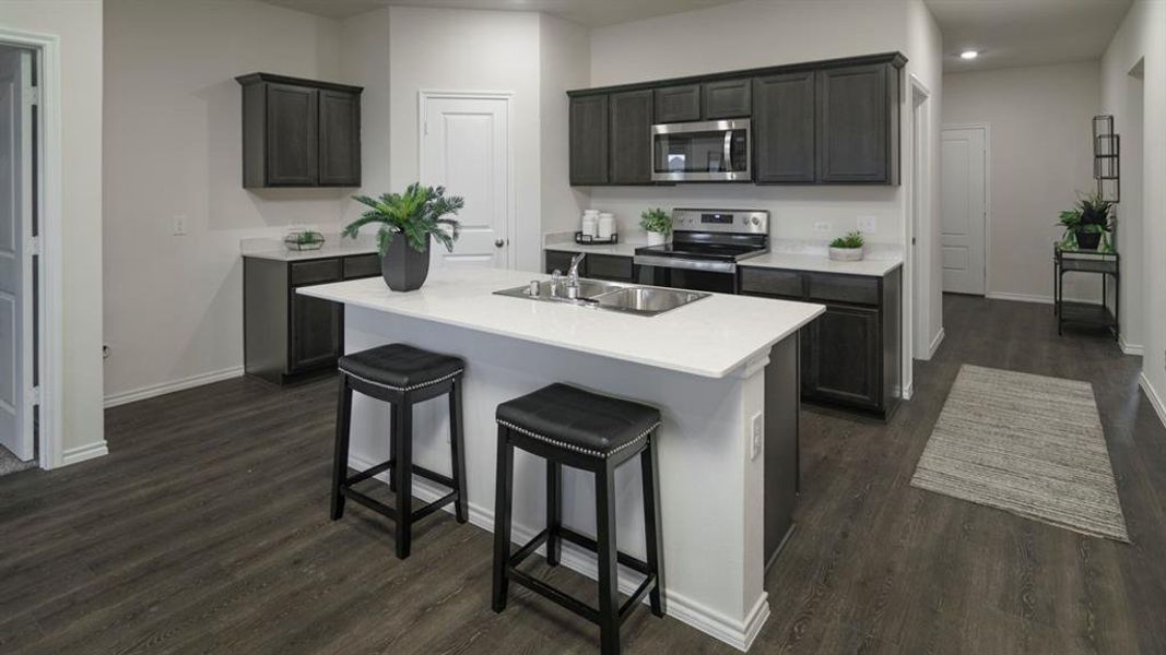 Open-concept kitchen featuring dark wood cabinetry, stainless steel appliances, a center island with sink, white countertops, and wood-finish flooring Open-concept kitchen featuring dark wood cabinetry, stainless steel appliances, a center island with sink, white countertops, and wood-finish flooring