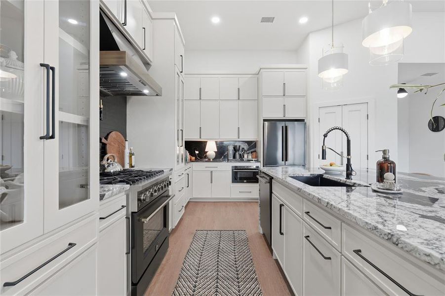 Gourmet kitchen featuring a gas range with stainless steel hood, built-in microwave, integrated refrigerator, and island with a black basin sink