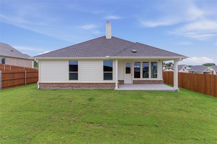Expansive rear lawn featuring a covered patio, brick and siding exterior, a dark shingled roof, and a privacy fence
