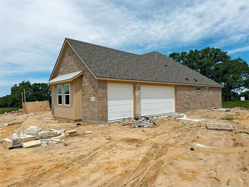 View of home's exterior featuring brick siding, roof with shingles, and a garage