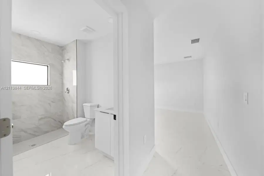 Bathroom featuring large-format light-toned tile flooring, walk-in shower with stone-style wall surround, transom window, and white cabinetry Bathroom featuring large-format light-toned tile flooring, walk-in shower with stone-style wall surround, transom window, and white cabinetry