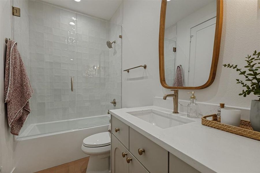 Bathroom featuring a single vanity with a white countertop and undermount sink, brass-finish faucet, and light gray cabinetry with brass-finish hardware Bathroom featuring a single vanity with a white countertop and undermount sink, brass-finish faucet, and light gray cabinetry with brass-finish hardware