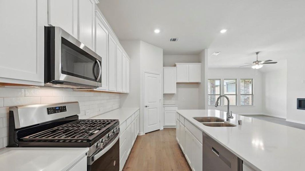 Kitchen featuring white shaker cabinetry, stainless steel appliances, a subway tile backsplash, and a large island with an undermount dual-basin sink
