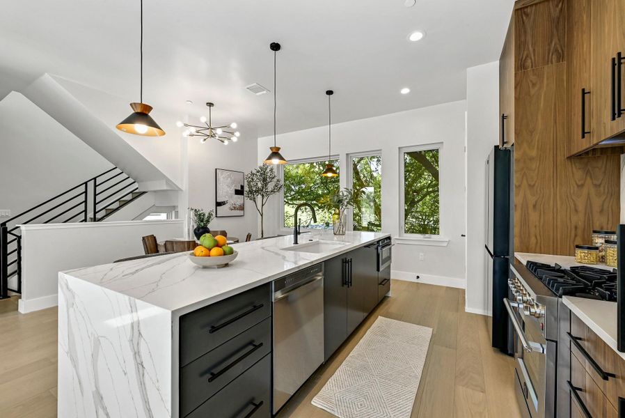Kitchen featuring custom wood cabinets, quartz waterfall countertop with breakfast bar area, and high end stainless steel appliances. (This is Unit #2 - each Unit has the same layout, however a few differing details such as light fixtures, custom cabinet/backsplash/tile colors)