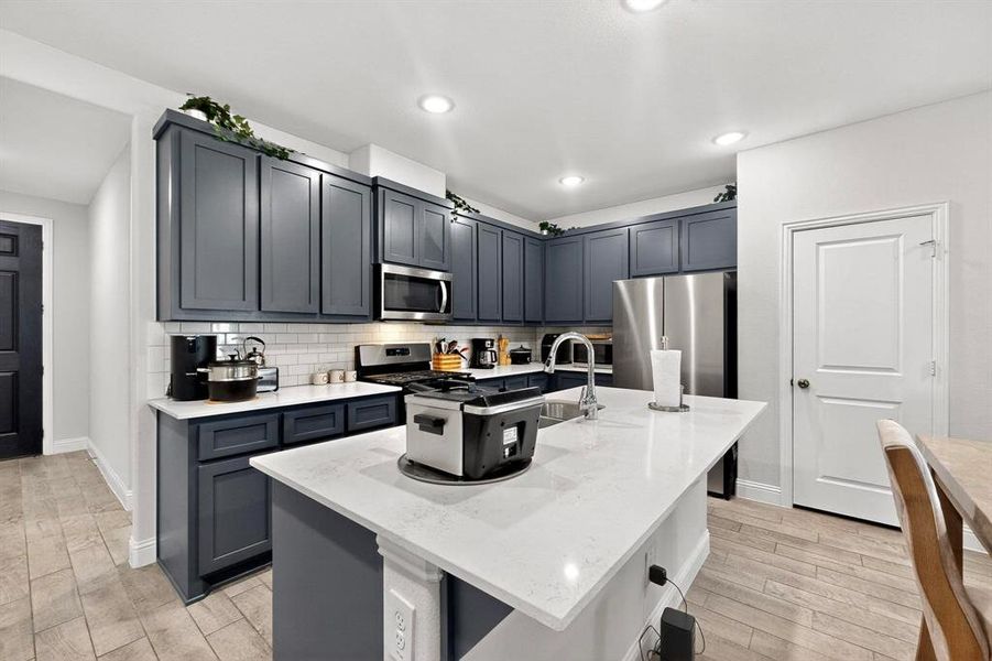Kitchen with wood finish floors, tasteful backsplash, light stone countertops, appliances with stainless steel finishes, and gray cabinetry Kitchen with wood finish floors, tasteful backsplash, light stone countertops, appliances with stainless steel finishes, and gray cabinetry