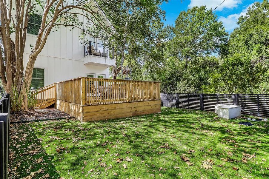 A spacious backyard features a sizable deck for outdoor enjoyment, framed by mature trees and a modern fence.