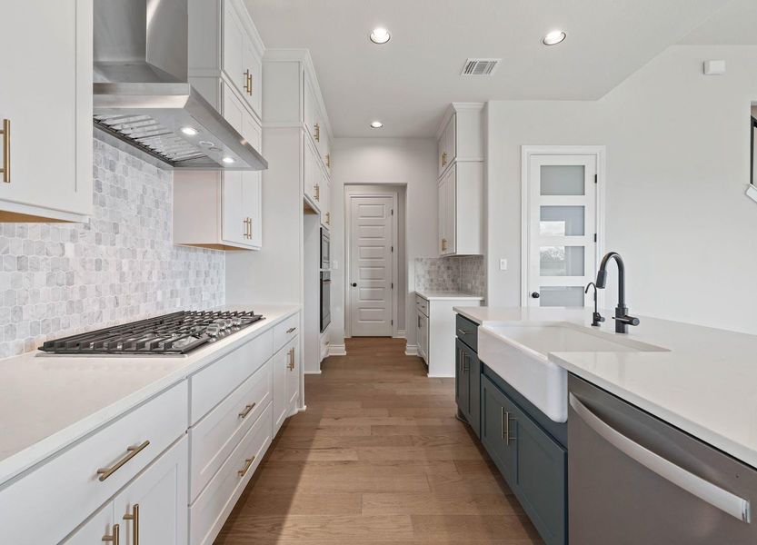 Kitchen featuring a sink, stainless steel appliances, wall chimney exhaust hood, visible vents, and white cabinets Kitchen featuring a sink, stainless steel appliances, wall chimney exhaust hood, visible vents, and white cabinets