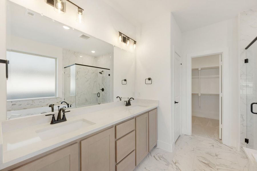 Master bathroom with double vanity, marble tile floors, glass shower, and walk-in closet entrance