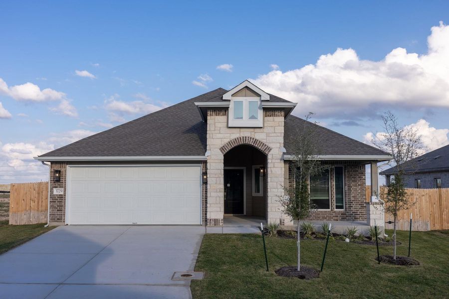 French country inspired facade with a shingled roof, concrete driveway, brick siding, and stone siding