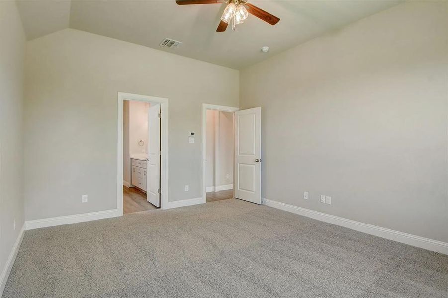 Unfurnished bedroom featuring light colored carpet, baseboards, ensuite bathroom, lofted ceiling, and ceiling fan