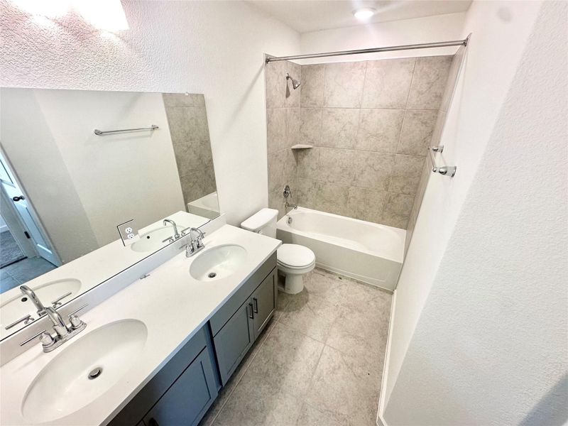 Full bath with double vanity,  shower combination, and a textured wall