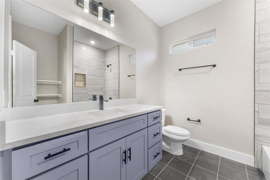 Bathroom featuring vanity, toilet, tile patterned flooring, and a tile shower