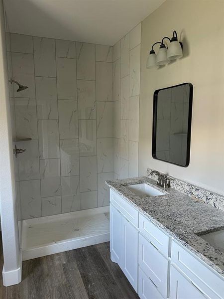 Full bathroom with a shower stall, double vanity, and dark wood-type flooring Full bathroom with a shower stall, double vanity, and dark wood-type flooring