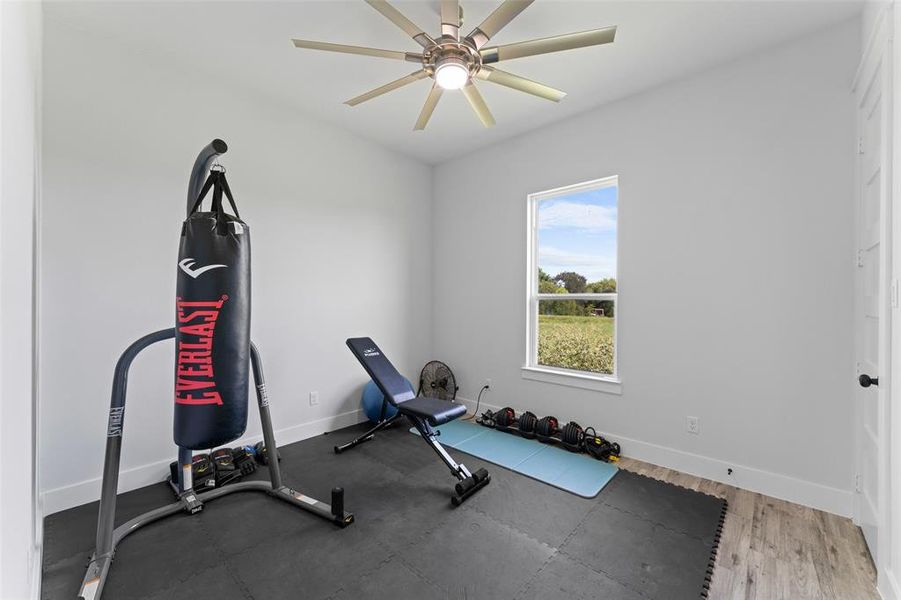 Versatile room featuring light grey walls, wood-finish flooring, and a ceiling fan with integrated lighting